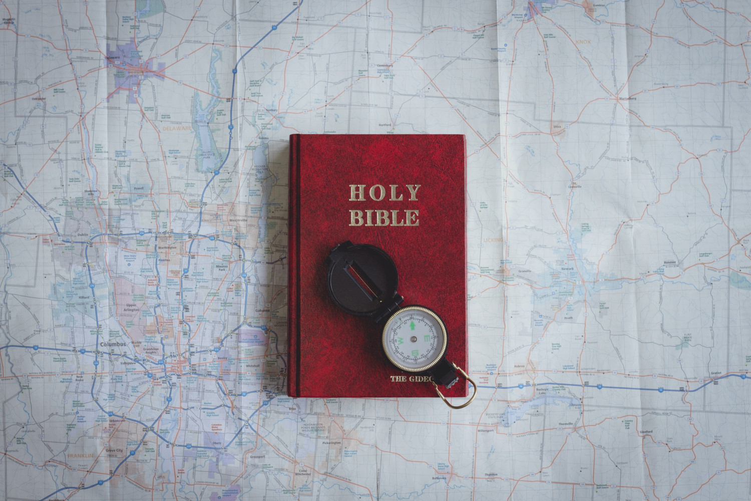 A map with a Bible on top of it. On top of the Bible is an old fashioned compass.
