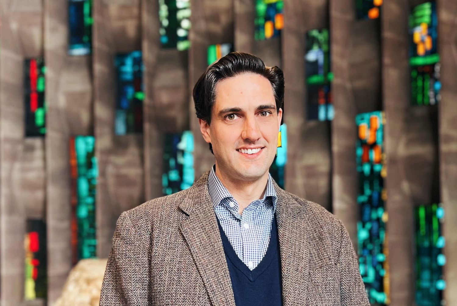 Matthew, a white man with brown hair, stands in front of a stained glass window at Coventry Cathedral.